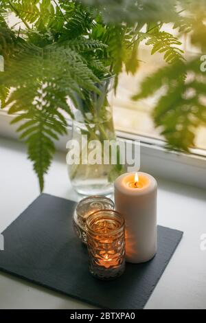 Isottaion soi-même, rester à la maison, vie intime : bouquet de fougère, bougie sur le rebord de la fenêtre. Concept de détente au calme et au calme, week-end saisonnier, spa, Banque D'Images