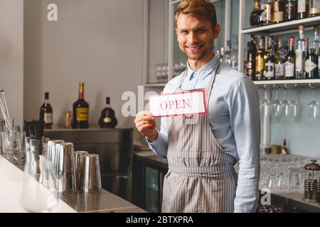 Barman gai dans un tablier tenant une affiche ouverte Banque D'Images