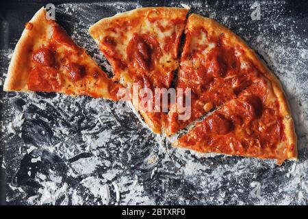 Quatre tranches de pizza poivrière fraîchement préparées sont sur une plaque de cuisson, saupoudrées de farine. Cuisine maison. Banque D'Images