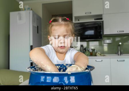 enfant preschooler joue dans la cuisine avec de la pâte. fille a laissé tomber ses mains dans un grand pot et est heureux Banque D'Images