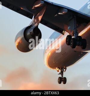 Avion prêt à atterrir ou à décoller au coucher du soleil, vue de dessous, gros plan de l'aile, du moteur et du châssis. Banque D'Images