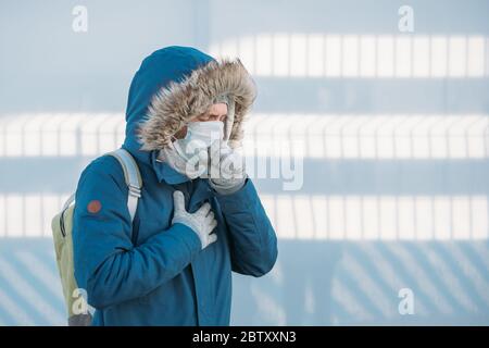 Portrait d'un jeune malade en blouson bleu mis sur une capuche, ayant un rhume, se sentir mal, toussant, portant un masque médical, à l'extérieur. Maladie, upcomi Banque D'Images