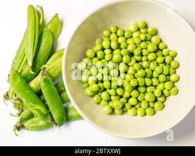 Un bol de petits pois fraîchement écossés et de gousses de pois vides d'en haut sur fond blanc Banque D'Images