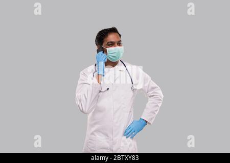 Médecin parlant au téléphone portant un masque médical et des gants. Indian Man Doctor avec téléphone isolé Banque D'Images