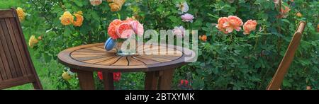 Séjour romantique dans le jardin de roses, round table et chaises en bois près des grands buissons à fleurs de roses anglaises Banque D'Images