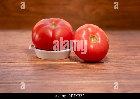 deux grandes tomates rouges fraîches sur une plaque en céramique blanche avec fond en bois Banque D'Images