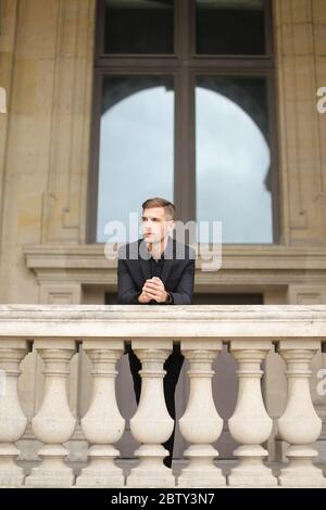 Jeune garçon assis sur une balustrade en béton de balcon à Paris. Banque D'Images