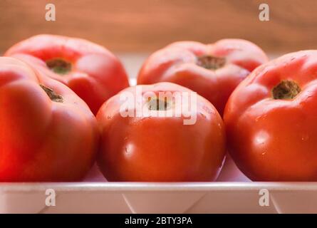 beaucoup de tomates rouges fraîches sur un plateau blanc du supermarché avec fond en bois Banque D'Images