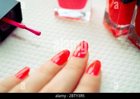 Doigts de femme avec manucure rouge, brosse et flacons en verre avec vernis à ongles sur une table blanche Banque D'Images