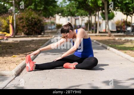 Jeune femme concentrée portant des collants et un débardeur qui étire sa jambe droite sur le sol sur un arrière-plan défocalisé. Concept de mode de vie sain. Banque D'Images