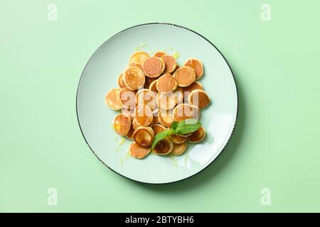 Petites crêpes aux céréales faites maison avec du miel dans une assiette verte sur fond turquoise. Vue de dessus. Petit déjeuner enfant savoureux. Banque D'Images
