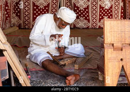 Charpentier omanais ou sculpteur de bois travaillant sur un repos de livre de coran appelé rehal dans le fort de Nizwa, Oman Banque D'Images