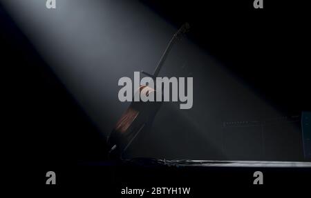 Une guitare acoustique reposant sur un stand sur une scène de concert de musique éclairée par un seul spot dramatique sur un fond sombre - rendu 3D Banque D'Images