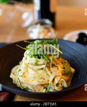 Recette italienne traditionnelle de pâtes Tagliatelle avec sauce aux truffes noires de champignons de la forêt, sauce carbonara au fromage blanc, servie dans un bo noir Banque D'Images