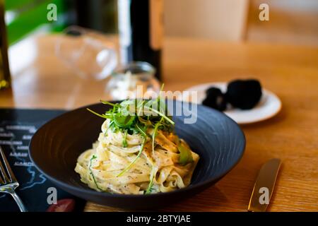 Recette italienne traditionnelle de pâtes Tagliatelle avec sauce aux truffes noires de champignons de la forêt, sauce carbonara au fromage blanc, servie dans un bo noir Banque D'Images