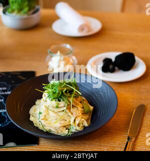 Recette italienne traditionnelle de pâtes Tagliatelle avec sauce aux truffes noires de champignons de la forêt, sauce carbonara au fromage blanc, servie dans un bo noir Banque D'Images