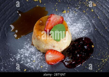 Riz au lait avec caramel sur le dessus. Fraises et assiette noire dans un cadre de restaurant. Dessert traditionnel italien original Banque D'Images