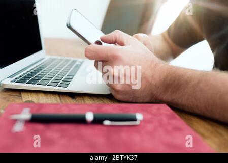 gros plan sur un homme utilisant un smartphone devant un ordinateur portable dans un bureau à domicile Banque D'Images