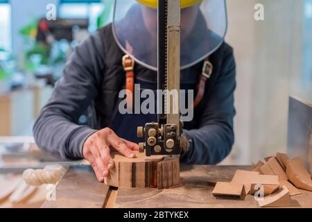 Carpenter coupe la pièce en bois par l'équipement sur le support. La main de l'homme fait un rond détail de la bûche. Le raccord utilise une scie électrique à métaux Banque D'Images