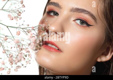 Floraison. Gros plan de la belle jeune femme avec des fleurs tendres sur fond blanc. Concept de cosmétiques, maquillage, traitement naturel et écologique, soins de la peau. Peau brillante et saine, mode, soins de santé. Banque D'Images