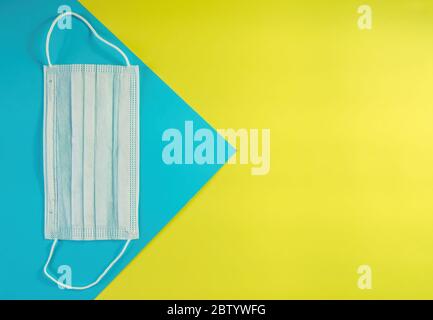 Masque médical blanc sur fond bleu et jaune. Protection contre le coronavirus, les allergies, la grippe. Masque de visage, vue de dessus, espace de copie Banque D'Images
