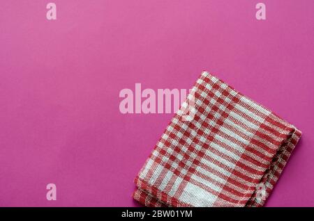 Fond rose clair avec une serviette à carreaux blanche et rouge. Serviette de cuisine pliée sur une table de couleurs. Arrière-plan minimaliste pour le multitâche. Vue de Banque D'Images