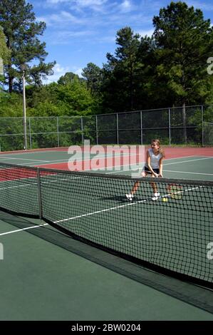 Le joueur de tennis universitaire de niveau secondaire se huste sur le net mais manque le ballon de tennis. Elle porte un skrt de tennis noir et un t-shirt blanc. La cour i Banque D'Images