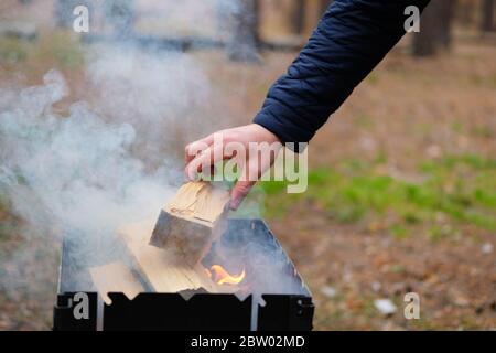 Saison de cuisson dans la nature ouverte. La main de l'homme ajoute du bois dans le feu. Barbecue en forêt. Banque D'Images