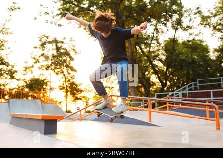 Jeune patineuse cool en T-shirt noir et jeans pratiquant des tours de saut sur planche à roulettes dans un parc de skate moderne Banque D'Images