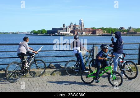 Enfants portant un masque sur des bicyclettes avec Ellis Island en arrière-plan pendant l'épidémie de coronavirus Covid-19.Liberty State Park.New Jersey.USA Banque D'Images