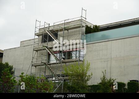 bâtiment résidentiel, moderne et petit avec échafaudage sur l'un des murs pour réparer le toit en terrasse avec quelques arbres au premier plan Banque D'Images