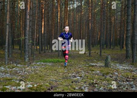 jeune femme qui fait du jogging dans une forêt de pins avec un sac à dos pour courir sur la piste Banque D'Images