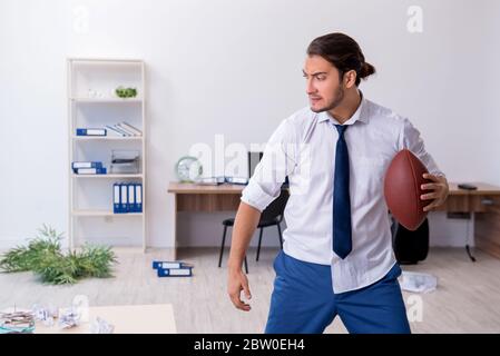 Jeune employé jetant du ballon de rugby dans le bureau Banque D'Images