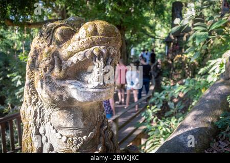 Sculpture d'une tête de dragon et touristes flous passant par dans le fond, au parc de la forêt de singes, Ubud, Bali, Indonésie Banque D'Images