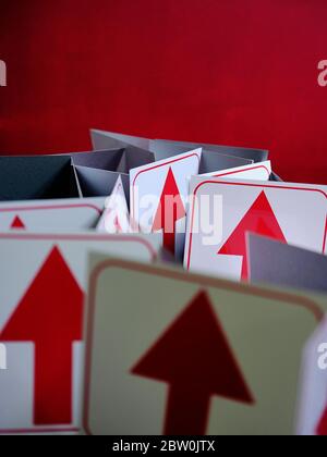Photo conceptuelle de flèches rouges directionnelles sur fond blanc contre un mur rouge vif. Banque D'Images