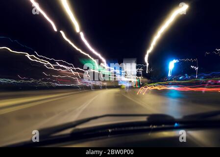 Une longue exposition et une vue boisée d'une voiture et les conducteurs qui se délcent sur la route la nuit. Banque D'Images