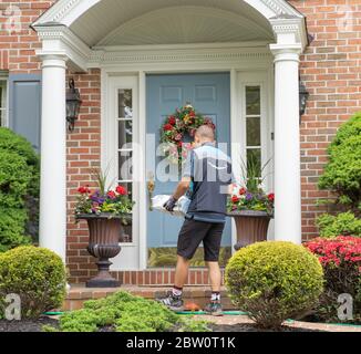 Berks County, Pennsylvanie, USA, 21 mai 2020, Amazon Delivery Person porte des gants livre le colis à la porte de la maison de banlieue. Banque D'Images