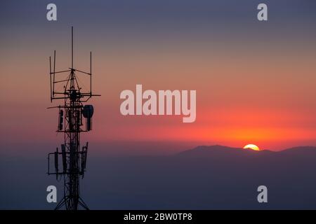 Tour de télécommunication avec arrière-plan de montagnes au coucher du soleil. Banque D'Images