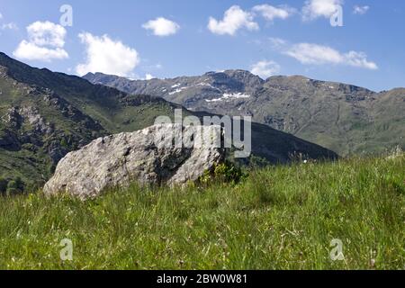 une grande pierre de granit reposant sur un pré avec les alpes en arrière-plan Banque D'Images