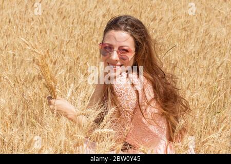 Voyage à la campagne. Beauté romantique fille appréciant la nature en plein air. Bonne jeune femme en robe de dentelle rose tenant les oreilles sur le domaine du ged Banque D'Images