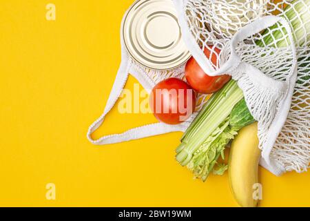 Livraison de nourriture. Aliments dans un sac à cordes sur fond jaune. Conserves alimentaires, tomates, concombres, bananes. Don, quarantaine du coronavirus. Su Banque D'Images