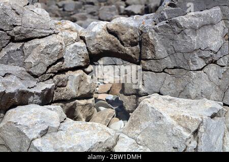 Une petite arcade de roche au milieu des rochers au bord de la plage montrant une arcade de roche fracturée avec un vide derrière elle. Banque D'Images