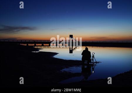 Un photographe fait la queue à la refuge Hut pendant le crépuscule astronomique sur la chaussée de l'île Sainte menant à l'île Sainte dans le Northumberland. Banque D'Images