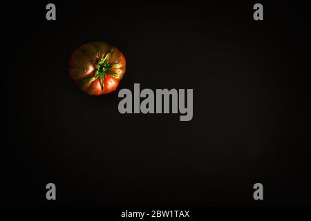 Une tomate isolée sur fond noir. Fruits naturels mûrissant. Non sélectionné, aspect naturel. Concept minimaliste. La règle des tiers de la photographie Banque D'Images