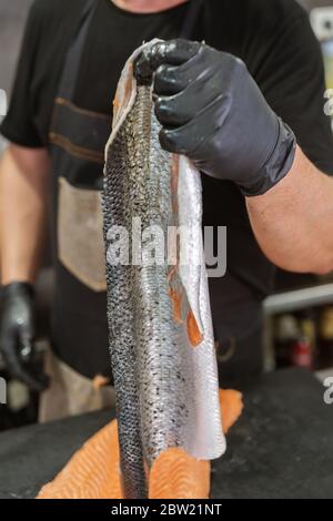 Master shusi avec des gants hygiéniques noirs pour le nettoyage et la préparation d'un énorme saumon frais. Retirer et peler la peau du poisson. Cuisine et cuisine conc Banque D'Images