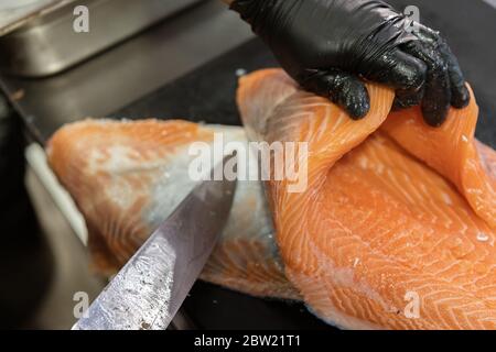 Master shusi avec des gants hygiéniques noirs pour le nettoyage et la préparation d'un énorme saumon frais. Retirer et peler la peau du poisson. Cuisine et cuisine conc Banque D'Images