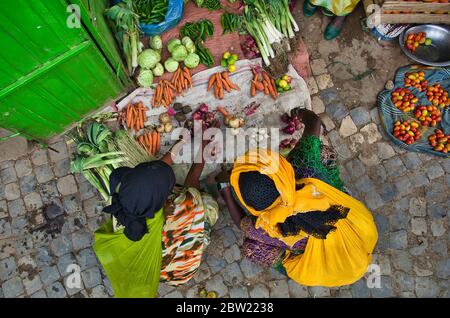 Des femmes noires en costumes traditionnels africains colorés qui se croisent sur un stand de légumes au sol et achètent des légumes. Prenez un zénith. Carottes, tomates Banque D'Images