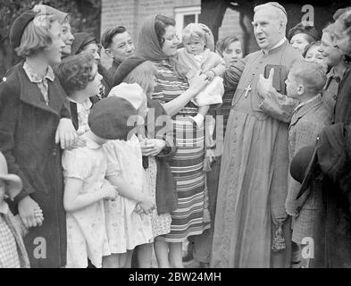 Embrasser l'anneau de l'Archevêque dans les jardins du houblon. L'archevêque de Southwark, le RT Rev P E Amigo, a fait sa visite annuelle dans les jardins du houblon de Kent aujourd'hui (dimanche) et a célébré une messe spéciale des cueilleurs de houblon à Horsmonden. Photos montre, l'archevêque, l'évêque, patrant la main du bébé après la messe. 4 septembre 1938 Banque D'Images