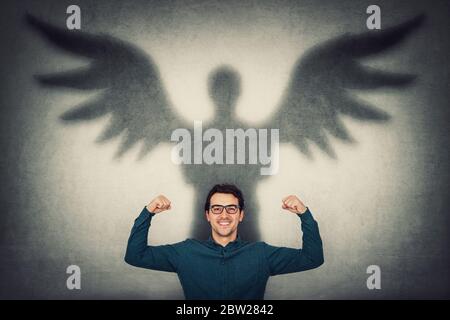Un homme d'affaires confiant et flexible imagine une superpuissance. Guy montre sa force, jetant une ombre de super-héros avec des ailes d'ange sur un mur. deve personnel Banque D'Images