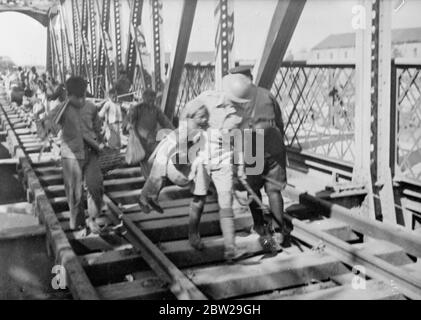 Briton s'est assuré de sauver une vie!. Les réfugiés se balanlent sur le pont alors que les Chinois se retirent de Shanghai. Un soldat britannique, avec un petit réfugié chinois sous son bras, traverse le pont ferroviaire de Jessiefield à Shanghai après qu'il ait été partiellement détruit par les Chinois en retraite. Le pont est sur le chemin de fer de Shanghai-Hangchow. Des milliers de réfugiés ont afflué sur le pont et martelé aux portes de l'établissement international en suppliant de s'y introduire. Parfois, les forces qui gardaient la frontière nord-ouest de la colonie étaient presque impuissantes contre les foules ravagées par la terreur qui ont balayé Banque D'Images